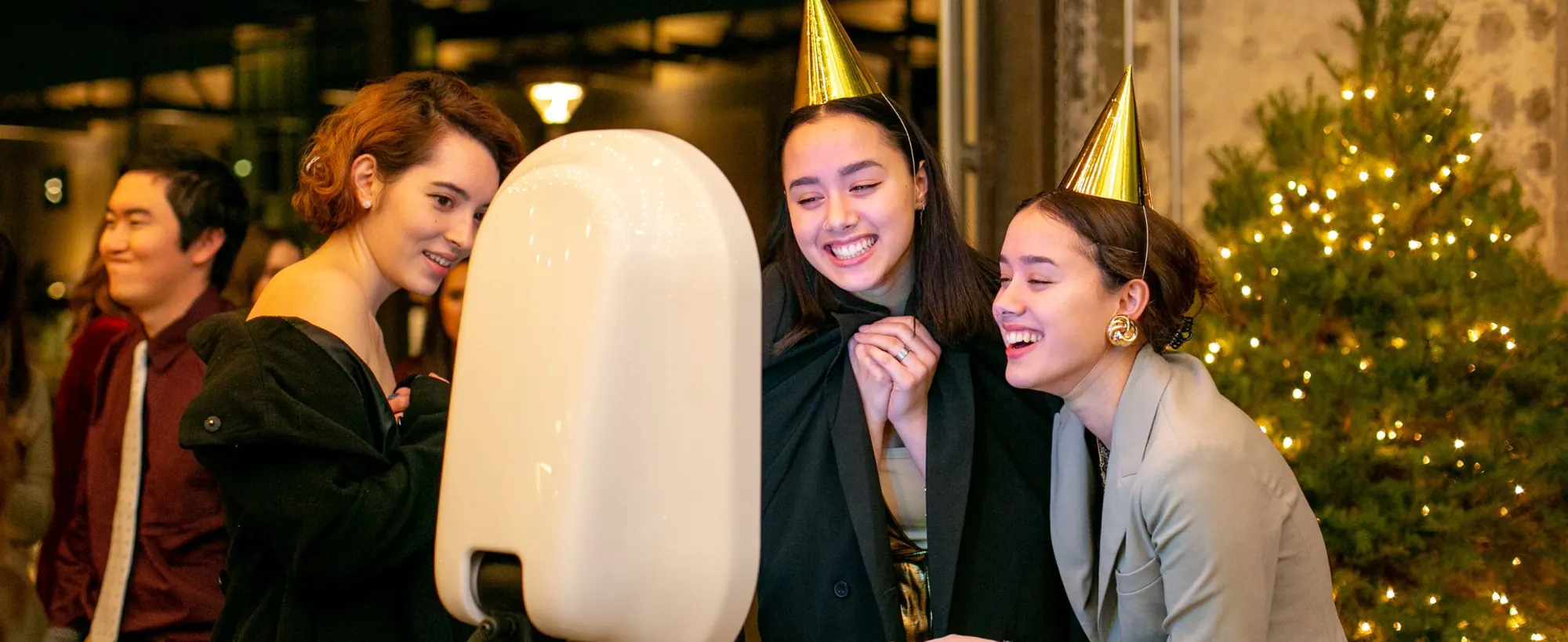 Friends in party hats gather around the In Flow booth beside a Christmas tree
